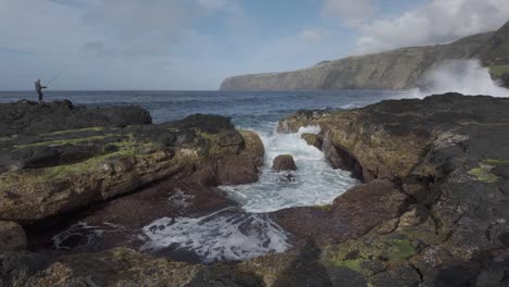 Lone-person-standing-on-rugged-volcanic-rocks-by-the-ocean-in-Mosteiros,-Sao-Miguel,-wide-shot
