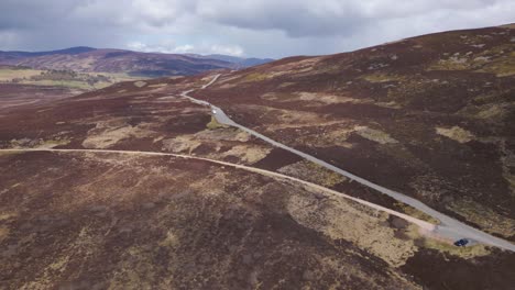 Aerial-flying-over-The-Cairngorms,-cars-traveling-by-road,-Scotland