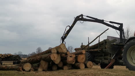 Tractor-unloading-logs-from-trailer-on-moody-day,-static-view