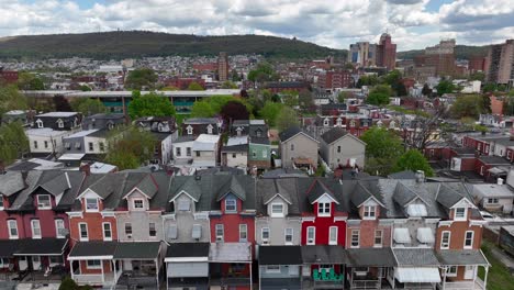 Aerial-view-of-a-colorful-row-of-townhouses-with-distinct-roofs,-in-a-dense-urban-setting-backed-by-a-hilly-landscape