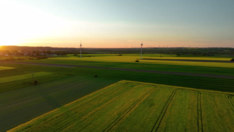 Expansive-green-fields-with-wind-turbines-at-sunset,-distant-village,-golden-light,-panoramic-view
