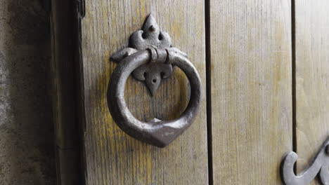 Detailed-closeup-of-metal-knocker-ring-on-worn-weathered-wooden-door