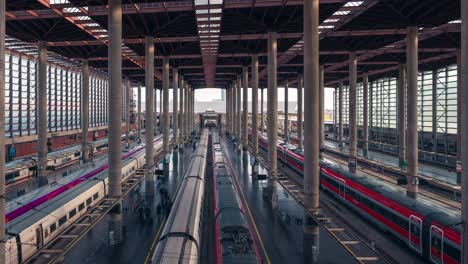 Left-to-right-pan-shot-of-Busy-atocha-railway-station-platforms-in-Madrid-during-sunny-day-high-Speed-trains-on-the-track-Passenger-traffic-on-the-platform-Fascinating-architecture-in-modern-train-hub