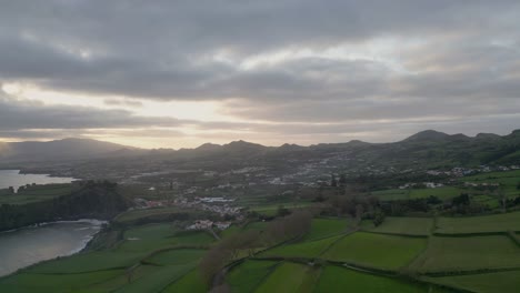 Luftaufnahme-Von-Ponta-Delgada-Auf-Den-Azoren,-Getaucht-In-Die-Warmen-Farbtöne-Eines-Atemberaubenden-Sonnenuntergangs,-Mit-Majestätischen-Bergen-Im-Hintergrund