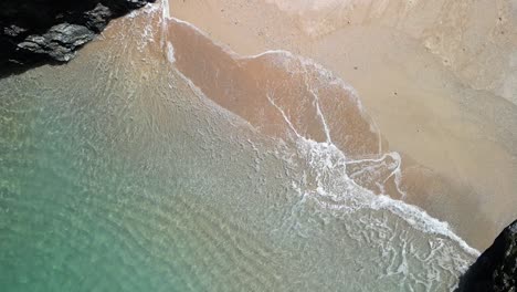 Cornish-Cove-In-Zeitlupe-Mit-Türkisfarbenen-Wellen,-Die-über-Einen-Strand-Rollen,-Aufsteigende-Drohne-Aus-Der-Luft,-Großbritannien