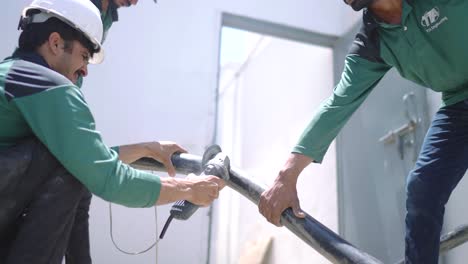 Engineer-Using-Angle-Grinder-To-Cut-Thick-Cable-Held-Up-By-Colleagues-At-Warehouse-In-Pakistan