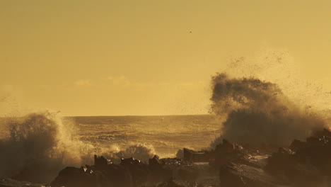 Olas-Del-Mar-Agitadas-Rompiendo-En-Las-Rocas-Creando-Un-Enorme-Rocío-Durante-La-Puesta-De-Sol-Dorada---Toma-Estática-Media