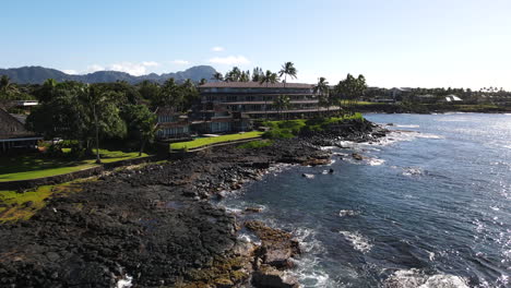 Aerial-Zoom-of-Poipu,-HI-Oceanfront-Luxury-Condos-with-Palm-Trees-and-Mountains