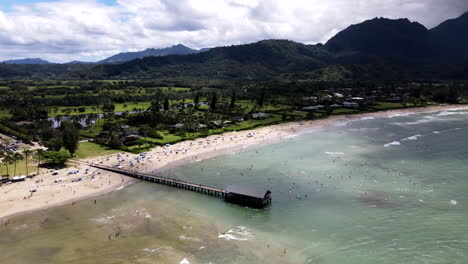 Aerial-Zoom-Out-from-Hanalei-Bay-with-Crowd-and-Pier-on-Cloudy-Day