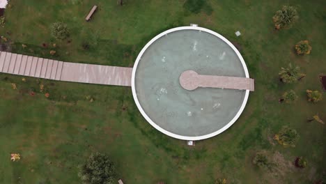 Aerial-view-of-a-circular-stone-structure-with-a-walkway-in-a-grassy-park-setting