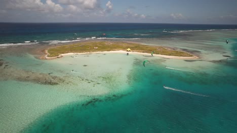 Mehrere-Kitesurfer-Rund-Um-Eine-Kleine-Insel-In-Los-Roques,-Venezuela,-An-Einem-Sonnigen-Tag,-Luftaufnahme