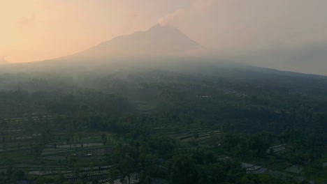 Smoking-Merapi-volcano-on-foggy-morning,-aerial-distant-view