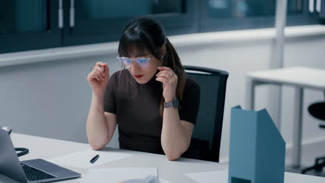 Close-up-of-a-young-beautiful-woman-with-dark-hair-working-on-papers,-being-tired-at-work-in-office,-having-a-migraine-in-slow-motion