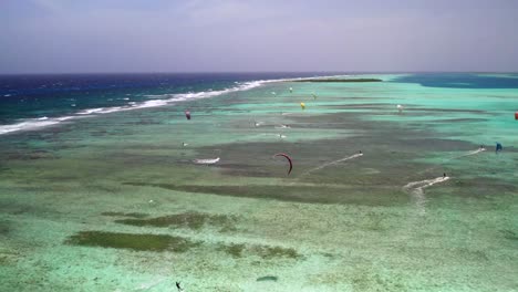 Kite-surfers-gliding-over-clear-turquoise-waters-by-sebastopol-barrier-at-los-roques,-aerial-view