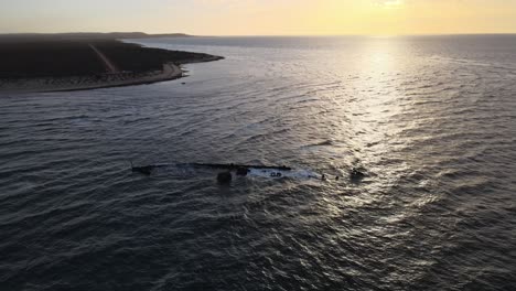 Drohnenluftaufnahme-Bei-Sonnenuntergang-über-Dem-Ozean,-Die-Zum-Schiffswrack-Hinunterschwenkt