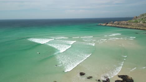 Scenic-Views-Over-Ocean-Waves-Along-Gwenver-Beach-with-Surfers-on-a-Summer's-Day,-Aerial-Panning-Shot,-Cornwall,-UK