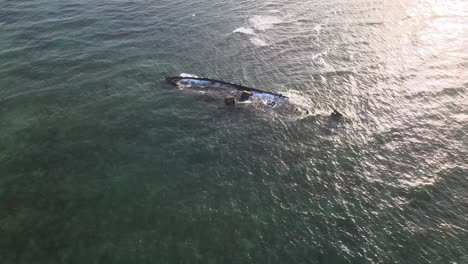 Drone-aerial-moving-slowly-over-waves-crashing-into-a-shipwreck-during-sunset