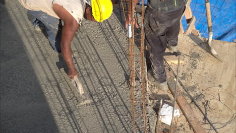 Tilt-down-shot-of-an-mexican-latin-construction-worker-with-a-hardhat-flattening-the-fresh-concrete-using-a-wooden-trowel-on-a-sunny-afternoon-in-slow-motion