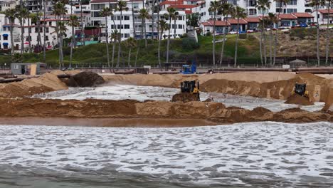 Bulldozers-moving-sand-on-a-beach-for-a-coastal-restoration-project,-San-Clemente,-2024