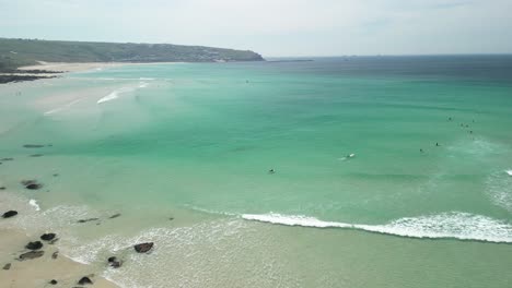 Gwenver-Beach-in-Cornwall-with-Surfers-Riding-the-Turquoise-Waves-with-an-Aerial-Drone-Panning-Shot,-UK