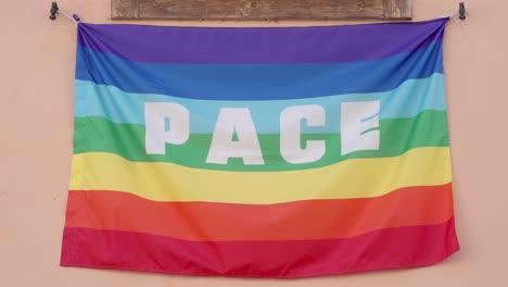 Eine-Italienische-Friedensflagge-In-Regenbogenfarben-Mit-Dem-Italienischen-Wort-„Pace“-Darauf-Hängt-Unter-Einem-Fenster
