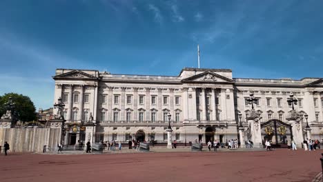 Vista-Frontal-Del-Palacio-De-Buckingham,-Con-Los-Visitantes-Reunidos-Delante-En-Una-Mañana-Soleada.