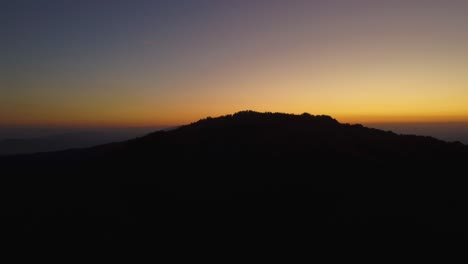 Aerial-reveal-of-mountain-silhouette-behind-the-hill-at-sunset