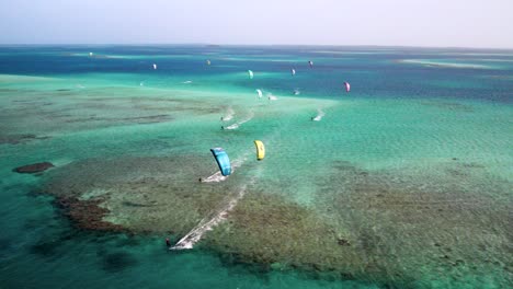 Multiple-kitesurfers-gliding-over-clear-turquoise-waters-at-los-roques,-cayo-vapor,-aerial-view