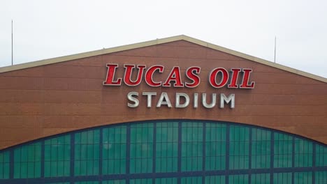 Luftaufnahme-Des-Indianapolis-Lucas-Oil-Stadium,-Das-Das-Branding-Auf-Der-Vorderseite-Der-Sportarena-Mit-Ziegelsteinfassade-Umkreist