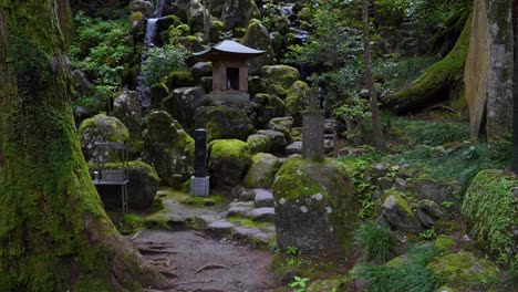 Filmischer-Schwenk-Nach-Oben-über-Einen-Wunderschönen-Wasserfall-Im-Asiatischen-Tempel-Im-Grünen-Wald