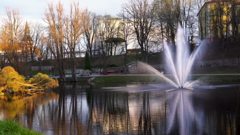 Scenic-fountain-in-Valmiera-park-by-Dzirnavu-lake,-Latvia-during-golden-hour-sunlight