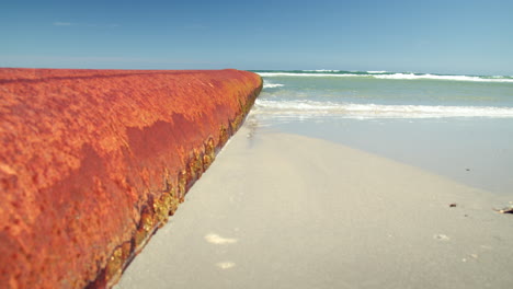 Wellen-Plätschern-In-Zeitlupe-An-Einem-Großen-Orangefarbenen-Rostigen-Rohr-Entlang