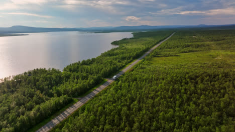 Aerial-view-of-a-camper-van-driving-remote-road,-moody,-summer-evening-in-Lapland