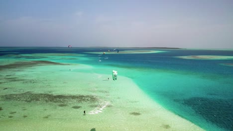 Kite-surfers-on-the-vibrant-waters-of-los-roques,-showcasing-the-dynamic-contrast-of-the-ocean,-aerial-view