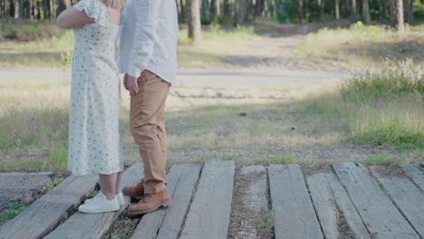 Couple-standing-together-on-wooden-pathway-in-a-forest,-focusing-on-their-legs-and-feet