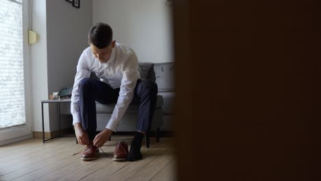 A-young-groom-sits-on-the-sofa-and-ties-his-shoes