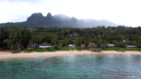 Zoom-Aéreo-A-La-Casa-De-Playa-De-Kauai-En-Un-Día-Nublado-Con-Montañas-Recortadas-En-El-Fondo