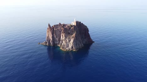 Cinematic-rotating-timelapse-drone-clip-around-a-rock-formation-natural-reserve-with-a-chapel-on-top-in-Strombolicchio,-Cicily,-Italy