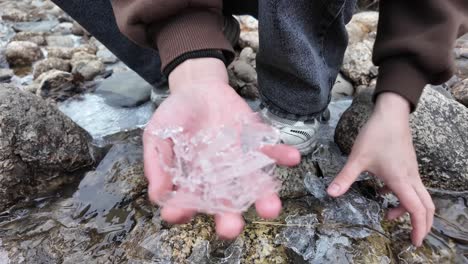 Hands-collecting-ice-shards-from-a-frozen-river,-creating-an-atmosphere-of-winter-nature-and-tranquility