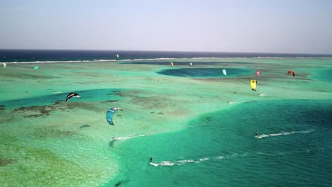 Multiple-kitesurfers-gliding-over-the-vibrant-reef-of-los-roques,-aerial-view