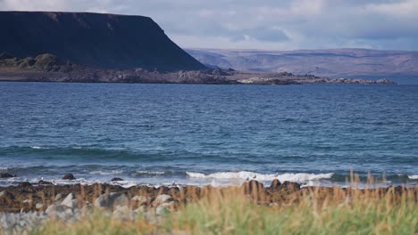 Waves-roll-slowly-on-the-rocky-grass-covered-beach