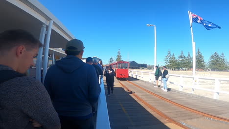 Travelers-patiently-wait-on-a-pier,-ready-to-embark-on-a-scenic-train-ride-at-busselton-jetty-under-the-clear-blue-sky