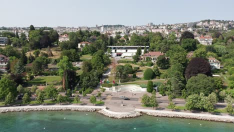 Drone-flying-over-lake-of-Geneva-towards-the-entrance-of-Olympic-Museum-in-Lausanne,-Switzerland-on-a-sunny-summer-day