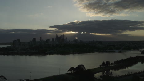 Skyline-Der-Stadt-Bei-Sonnenuntergang,-Wenn-Die-Sonne-Durch-Die-Wolken-Scheint-Und-Sich-Im-Wasser-Spiegelt