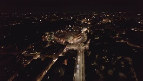 Aerial-static,-traffic-moving-around-the-Colosseum-at-night,-Rome