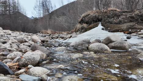 The-video-features-a-mountain-stream-flowing-among-large-rocks-in-a-winter-forest