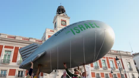 Pro-Palestine-protesters-gather-at-Puerta-del-Sol-in-Madrid,-Spain,-demanding-an-end-to-arms-sales-to-Israel,-with-some-holding-a-balloon-depicting-a-bomb-in-solidarity