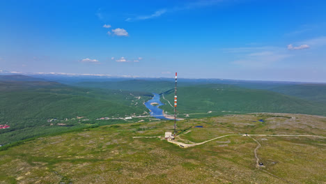 Aerial-tracking-shot-of-a-radiotower-on-a-mountain-summit-in-sunny-Utsjoki,-Finland