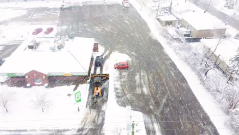 Heavy-machinery-cleaning-parking-lot-from-snow-during-extreme-blizzard,-aerial-view
