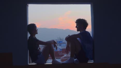 Romantic-couple-looking-each-other-sitting-in-window-at-sunset